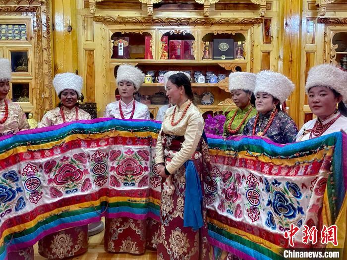 圖為女性展示村民自發(fā)繡制的“百米五彩哈達(dá)”?！±钣穹?攝